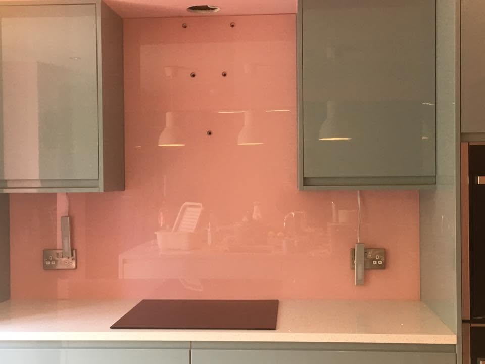 Pale pink glass splashback fitted between pale grey gloss kitchen cabinets