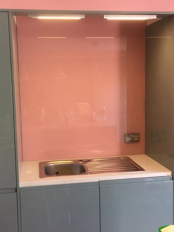 Coral pink glass splashback behind a stainless steel sink in a grey kitchen