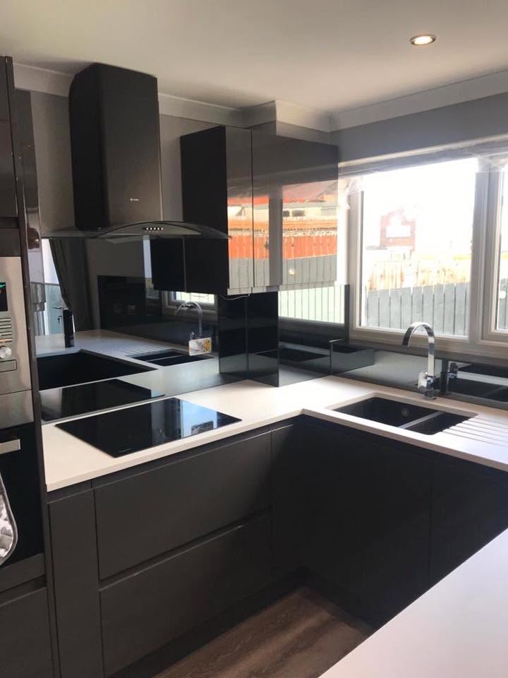 Black glass splashback behind a hob and sink in a dark grey and white kitchen