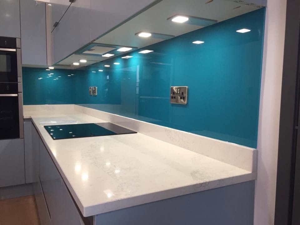 Bright turquoise glass splashback running the length of a white quartz kitchen worktop
