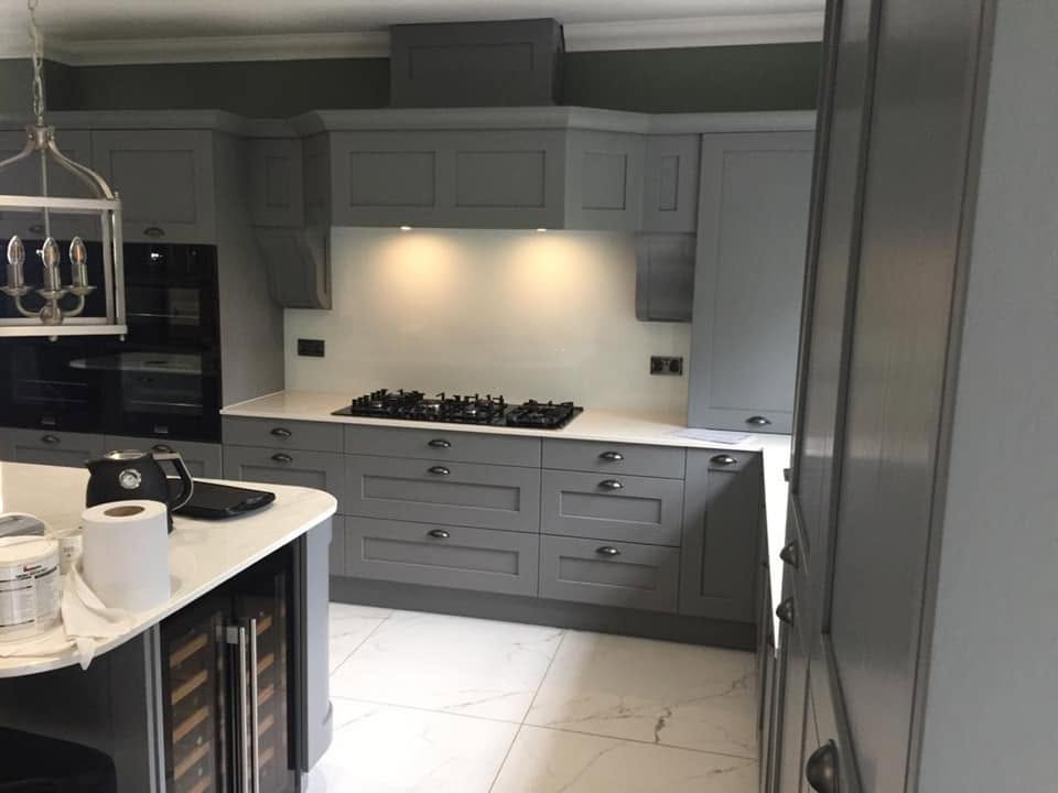 White glass splashback behind a gas hob in a traditional grey shaker kitchen