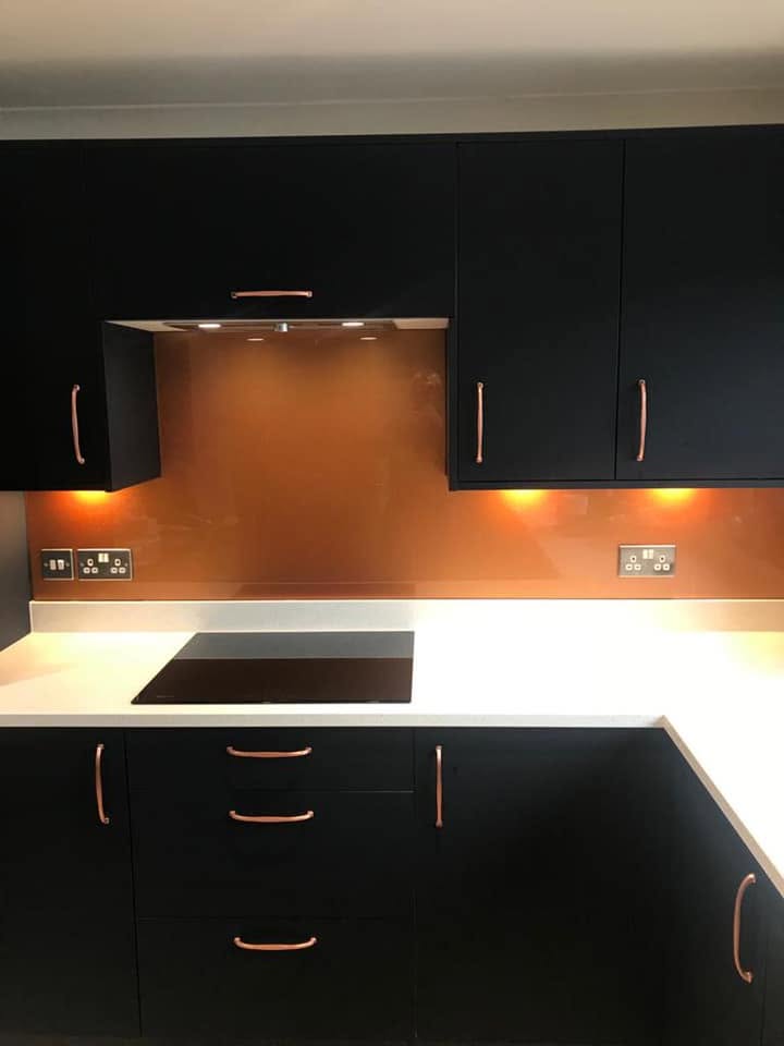 Copper bronze glass splashback behind an induction hob in a black matte kitchen