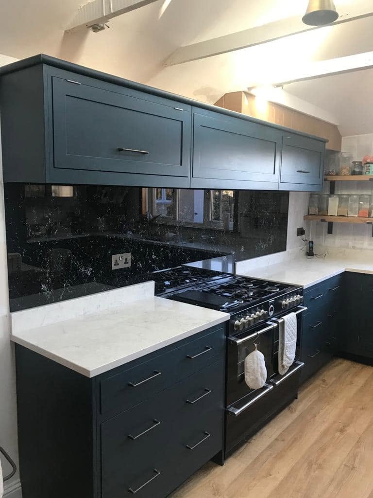 Black speckled glass splashback behind a range cooker in a navy shaker kitchen