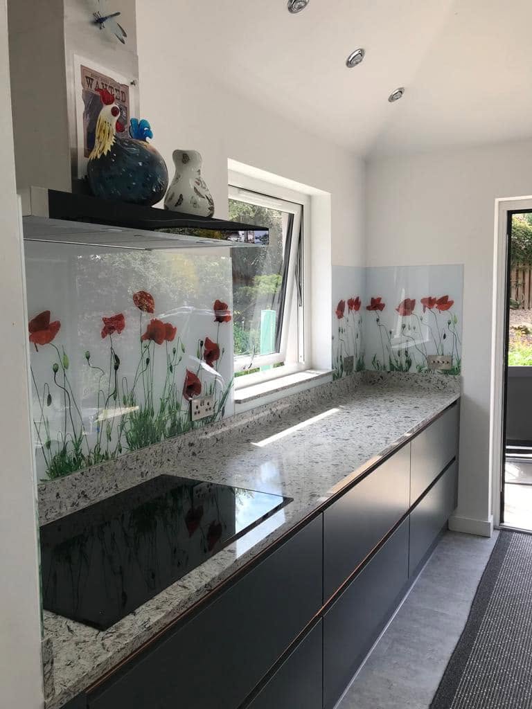 Printed glass splashback with a red poppy design along a granite effect worktop