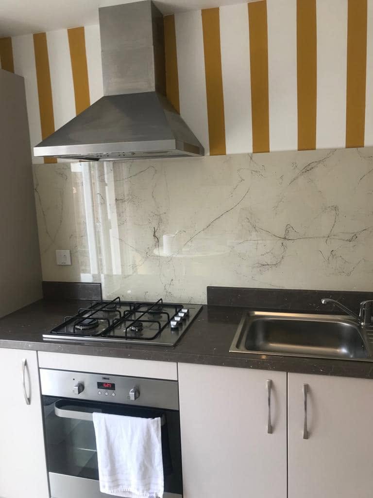 Marble effect glass splashback behind a hob and sink below mustard striped wallpaper