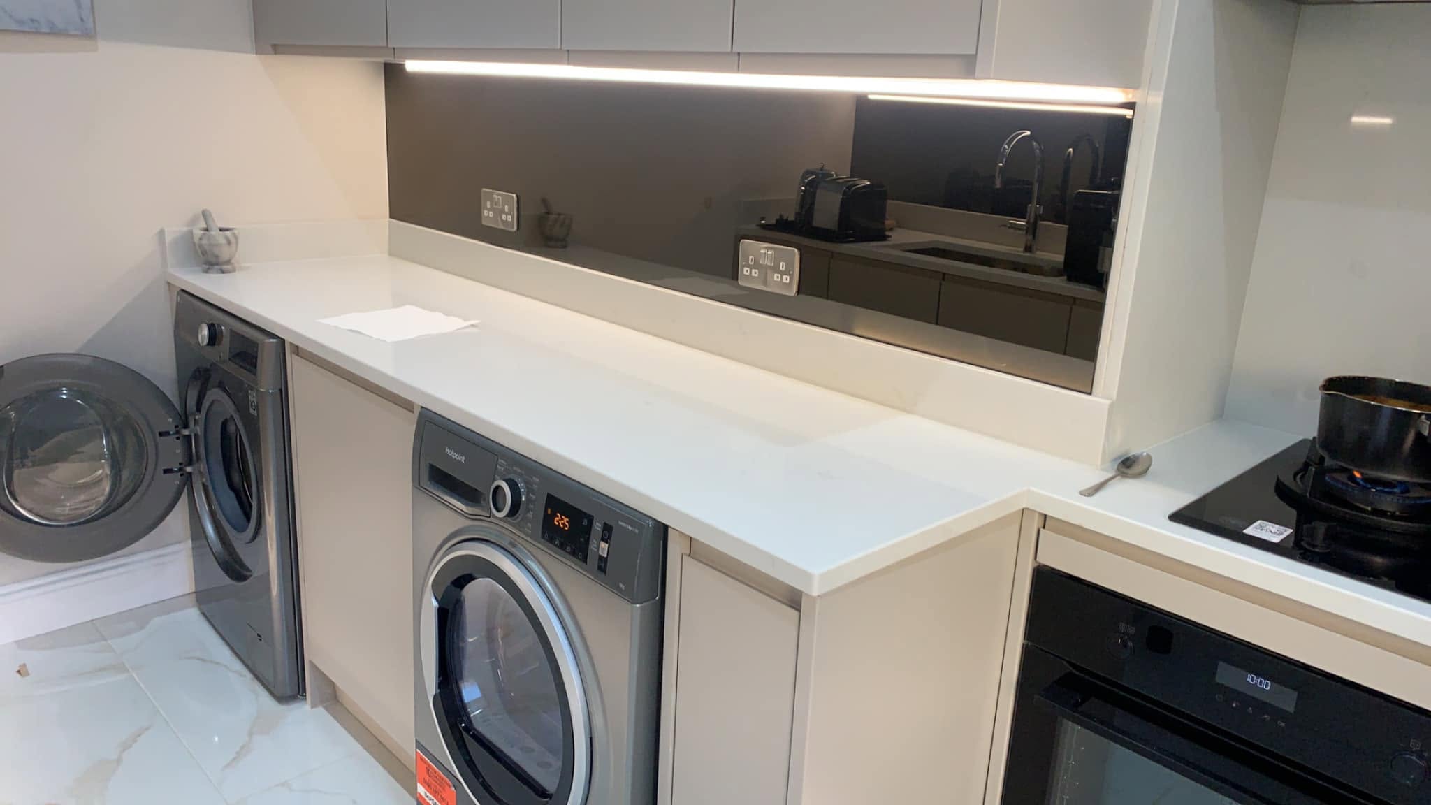 Bronze tinted mirror glass splashback above washing machines and a hob in a utility kitchen