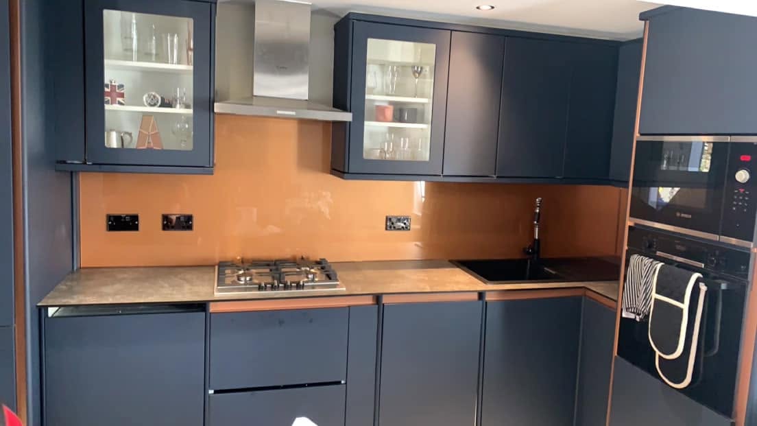 Copper toned glass splashback behind the hob and sink in a navy blue kitchen