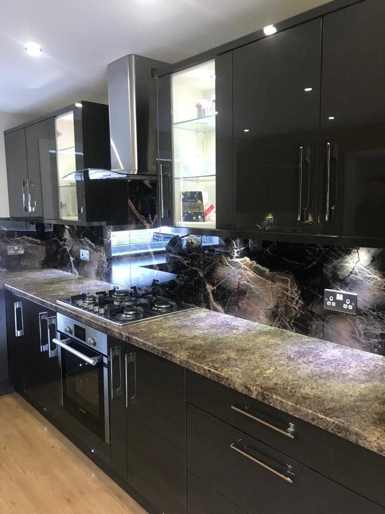 Marble effect glass splashback behind the hob in a black gloss kitchen