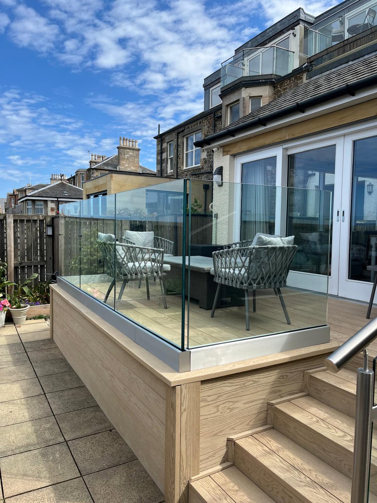 Frameless glass balustrade around a raised timber decking terrace with seating