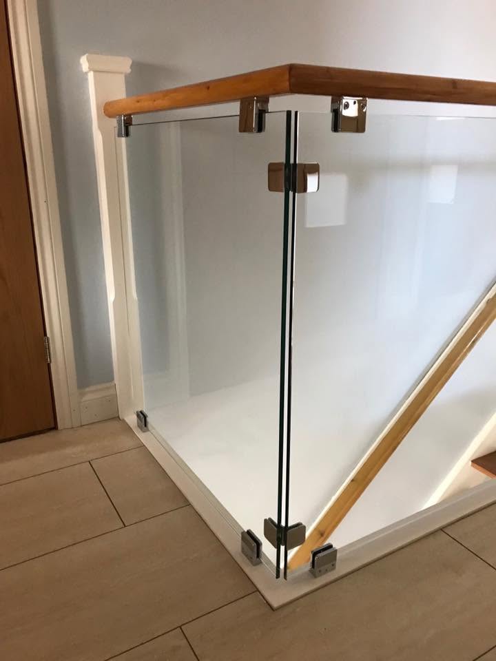 Glass balustrade panel with chrome clamps and timber handrail on a staircase