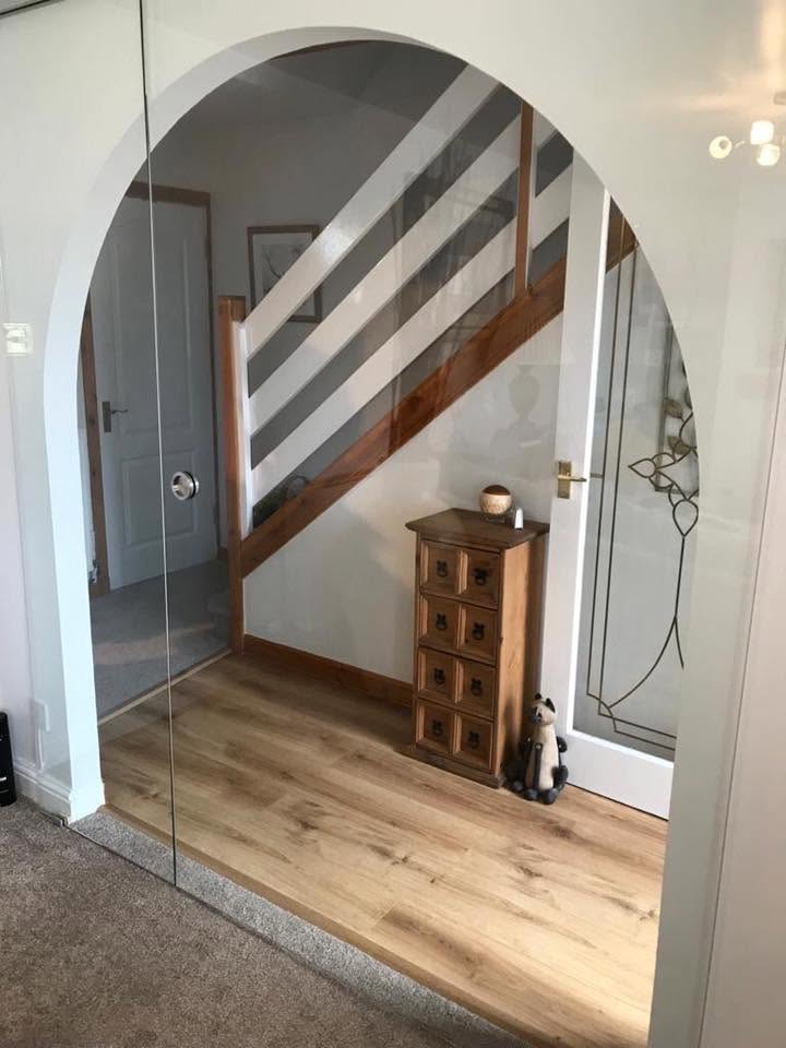 Frameless glass door fitted into an arched hallway opening with chrome handle