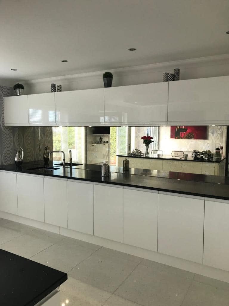 Mirrored kitchen splashback reflecting a white gloss kitchen with black worktops