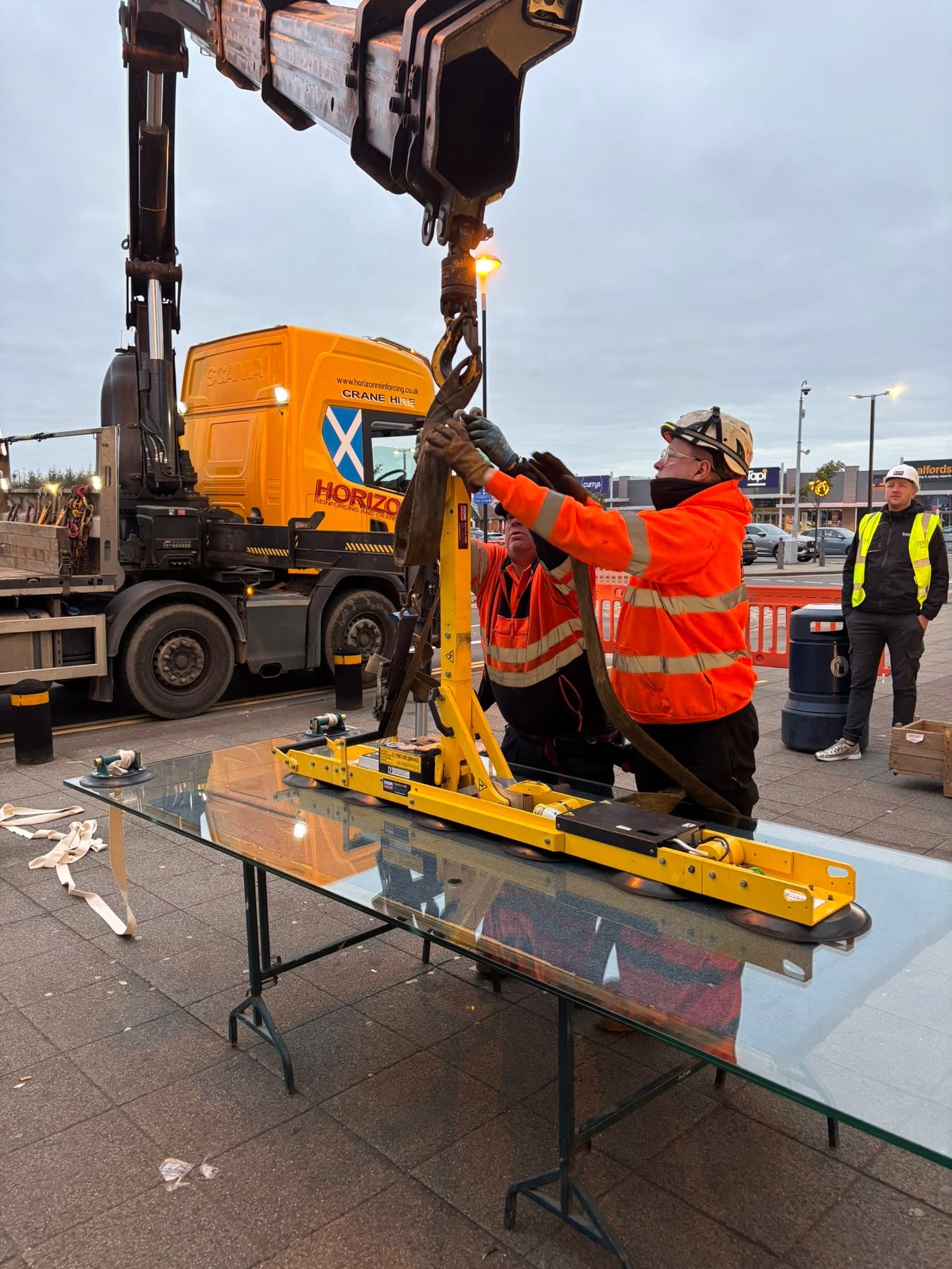 Crane and vacuum lifter installing a large glass pane on a shopfront