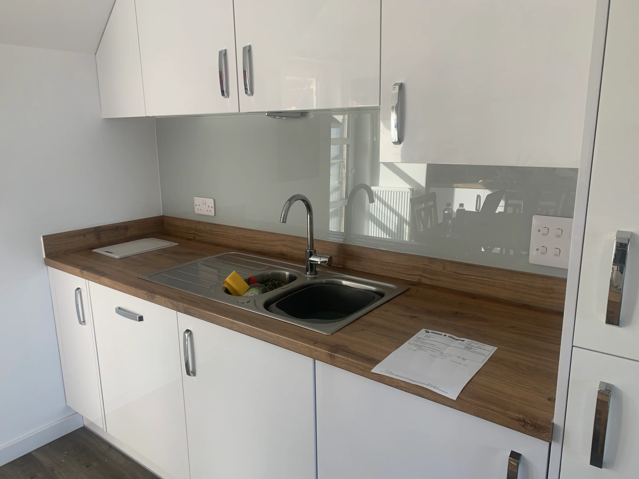 Grey glass splashback behind a stainless steel sink and wood effect worktop