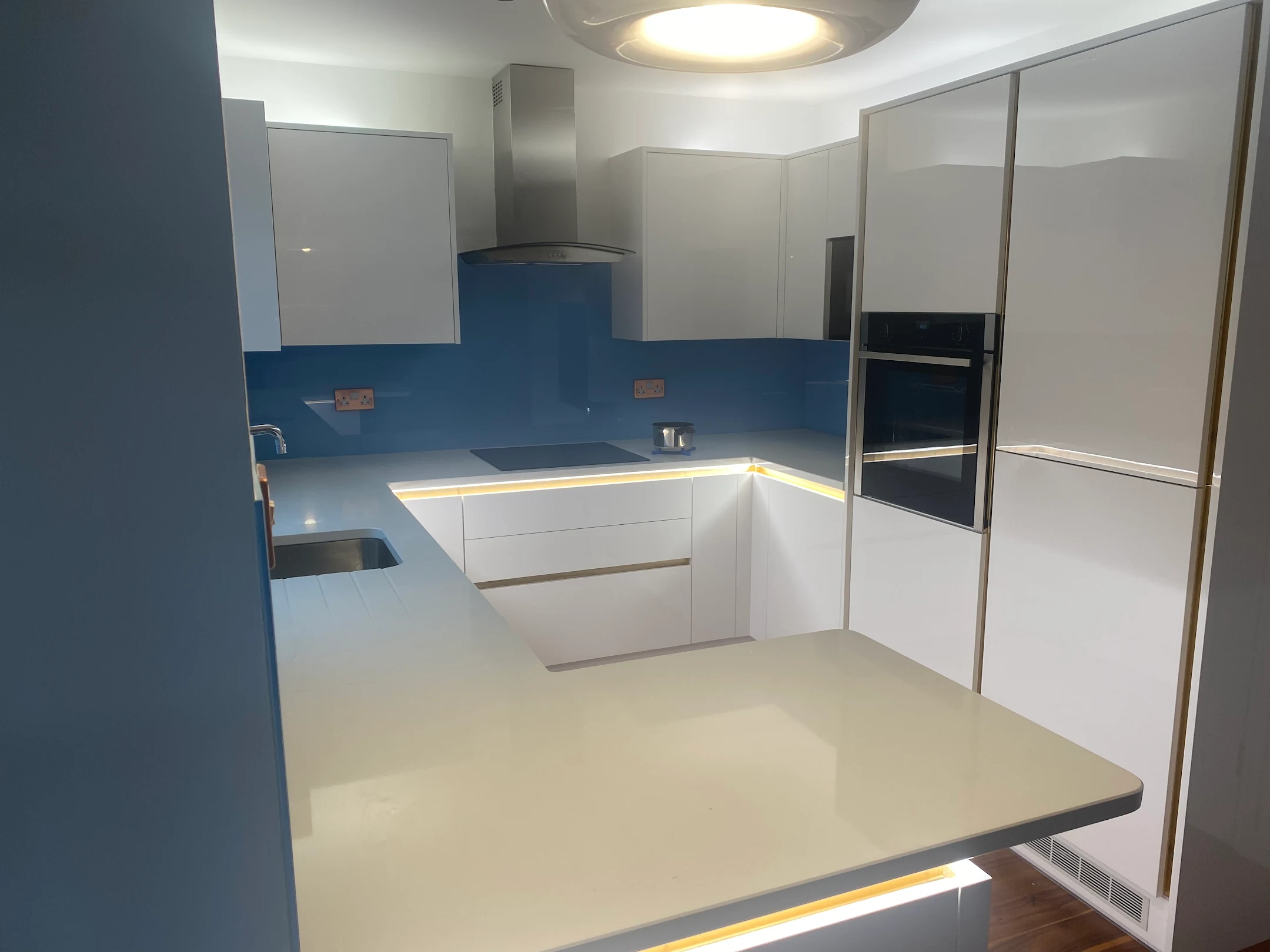 Bright blue glass splashback along the wall in a white gloss kitchen