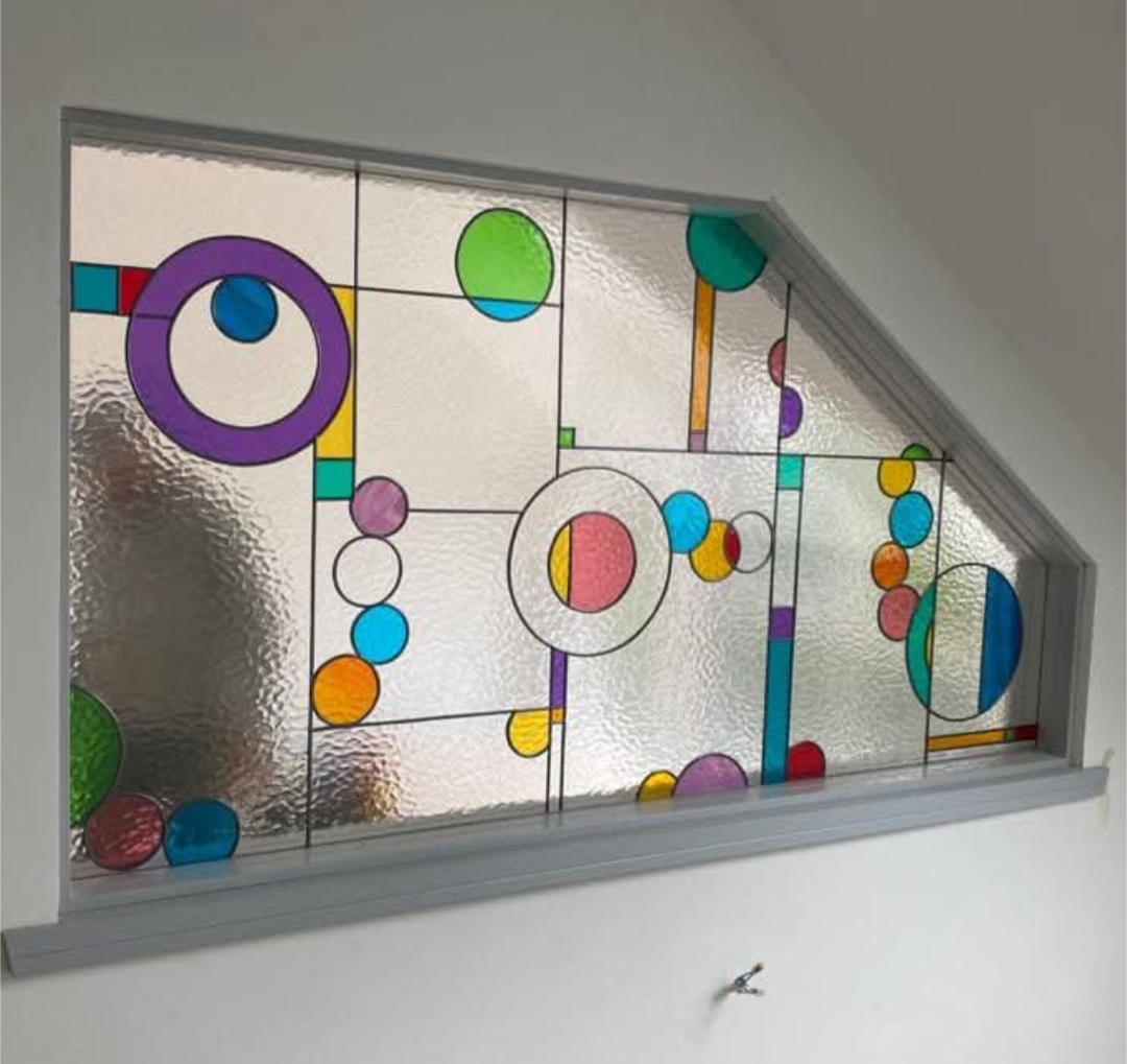Colourful stained glass window with circle and bubble shapes in an angled frame