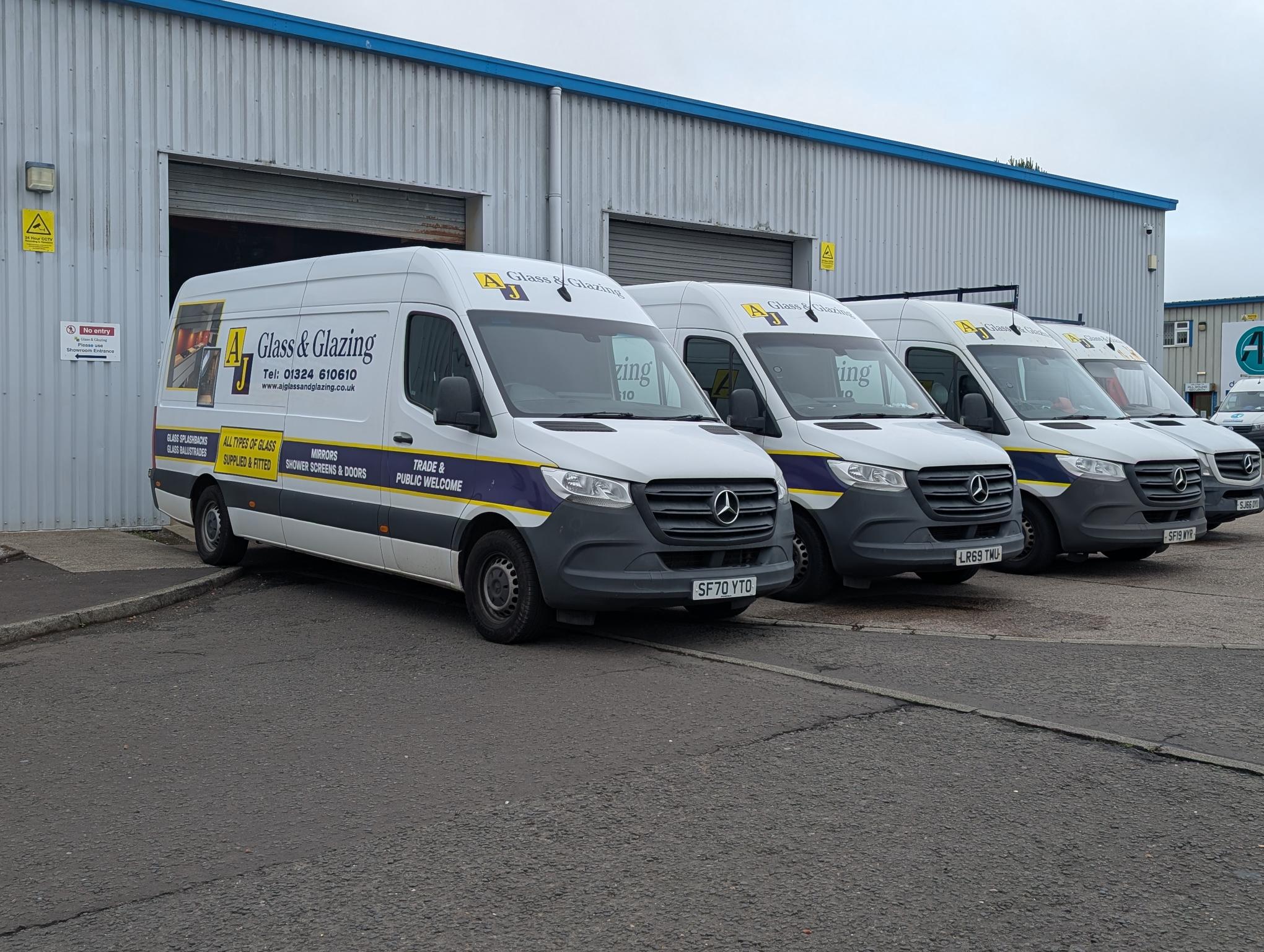 Row of AJ Glass and Glazing branded vans parked outside the workshop premises