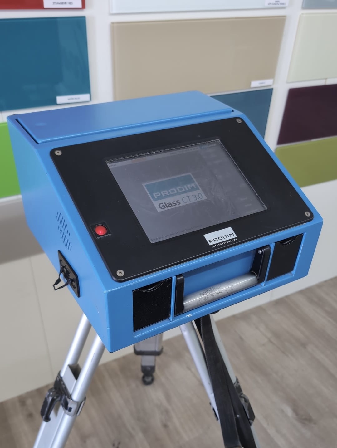 Prodim Proliner digital measuring tool on a tripod, with coloured glass splashback samples behind