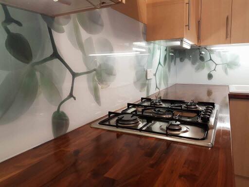 Printed glass splashback with a leaf design behind a gas hob and wooden worktop