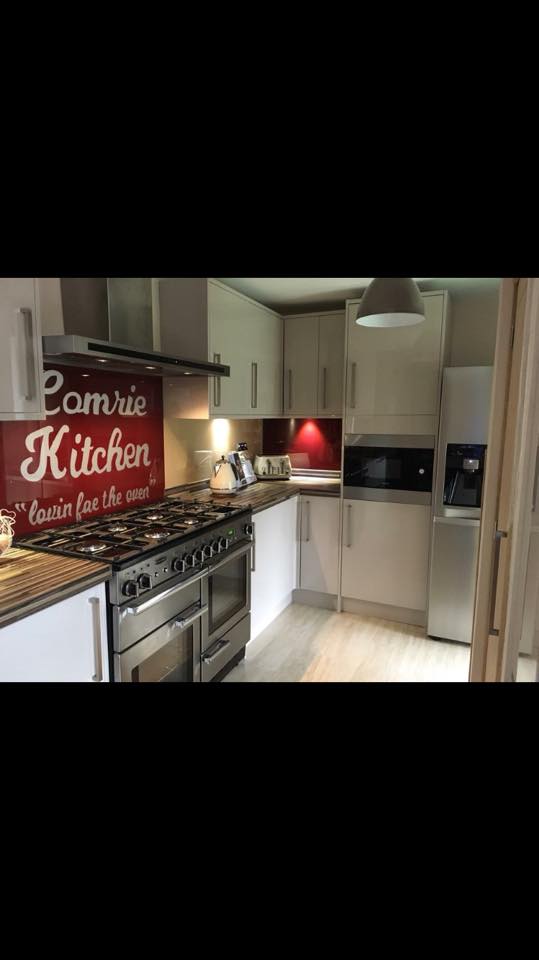 Red printed glass splashback with personalised kitchen text behind a range cooker