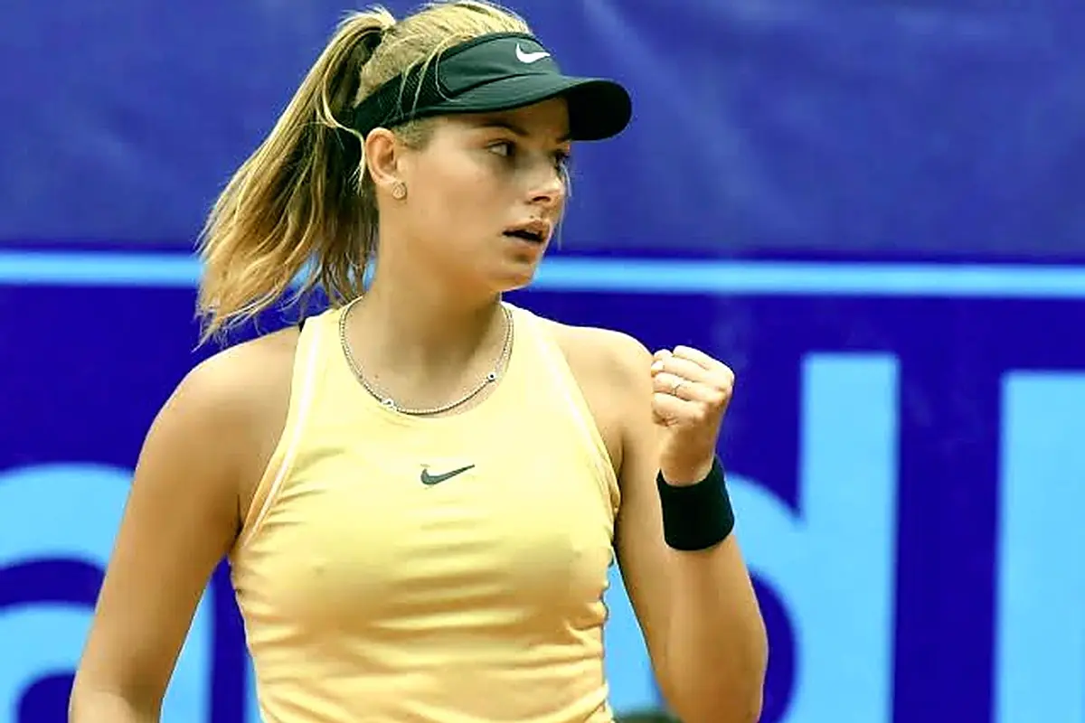 Female tennis player in a yellow Nike tank top and black visor showing a fist in focus.
