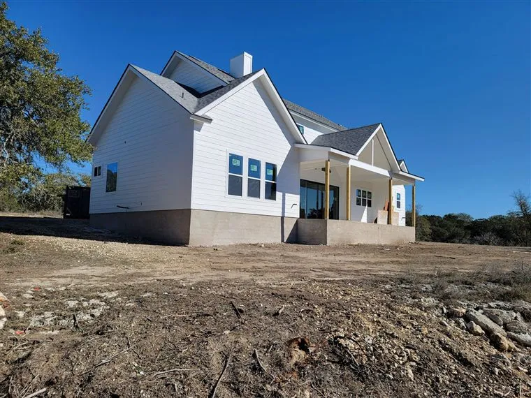 Newly built white board-and-batten custom home with gabled rooflines on a cleared Hill Country lot