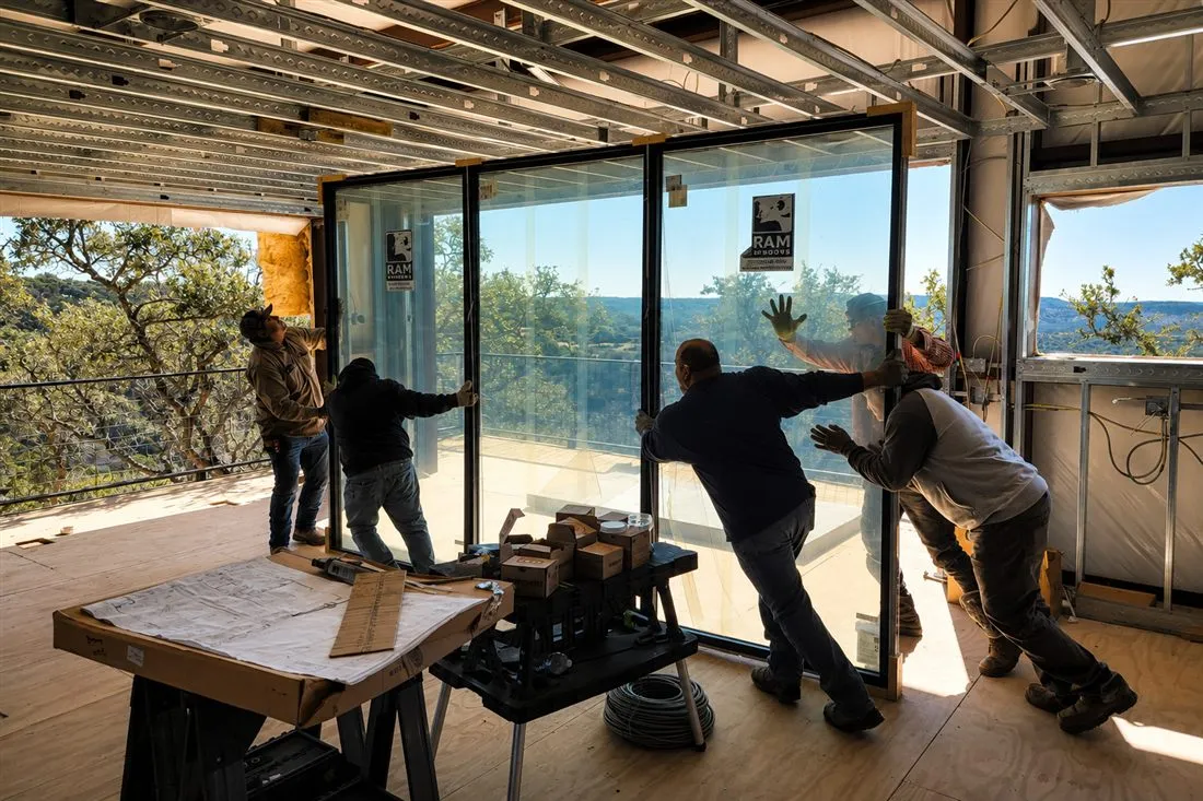 Crew installing a floor-to-ceiling sliding glass door wall in a home under construction overlooking the Hill Country