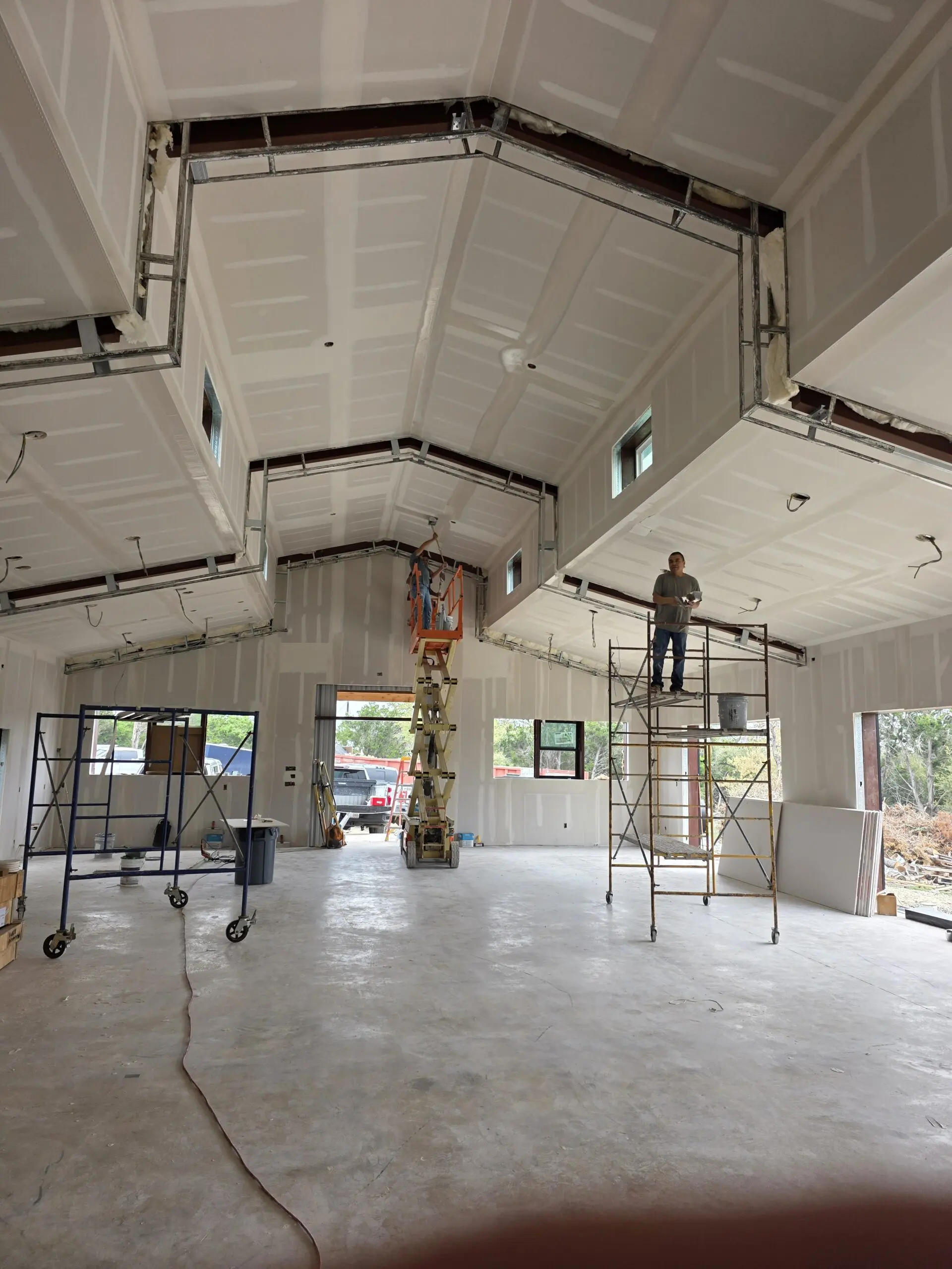 Worker finishing the vaulted interior of a steel-framed home over a bare concrete floor
