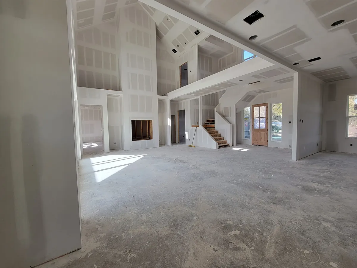 Drywalled two-story great room with a staircase and bare concrete floor, ready for owner finish-out