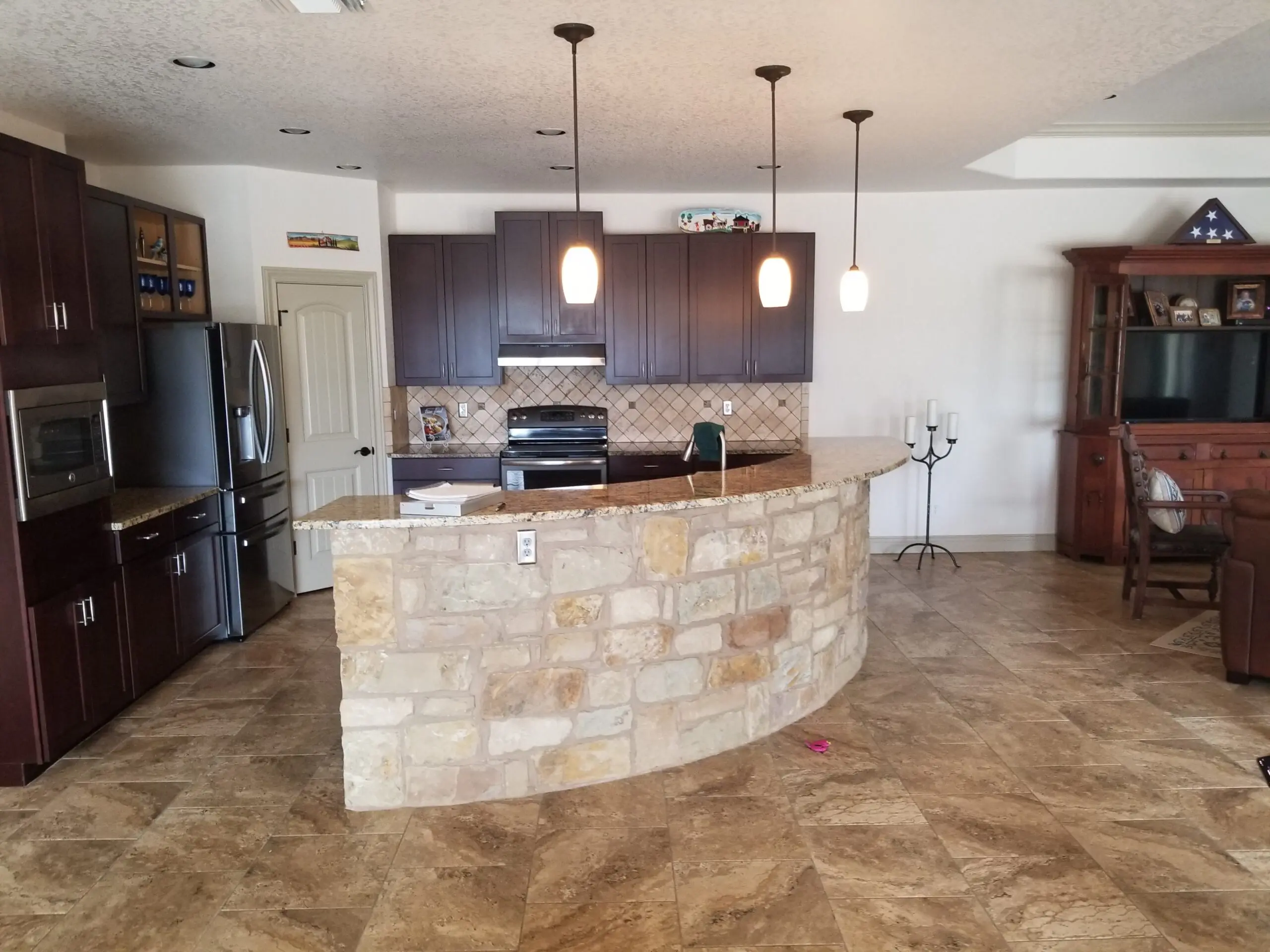 Finished custom home kitchen with a curved Hill Country limestone bar, granite countertops and dark wood cabinetry