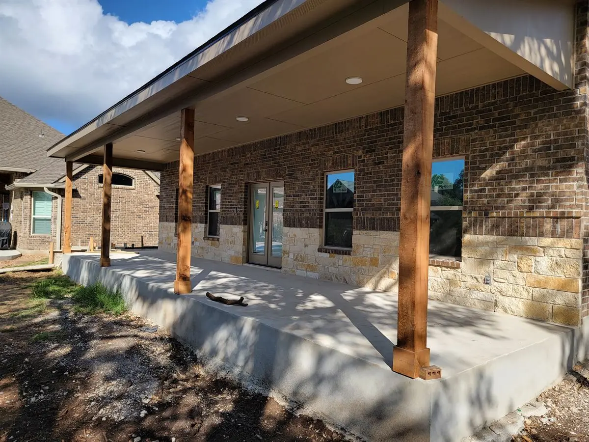 Covered rear patio with cedar posts and limestone accents on a finished brick home