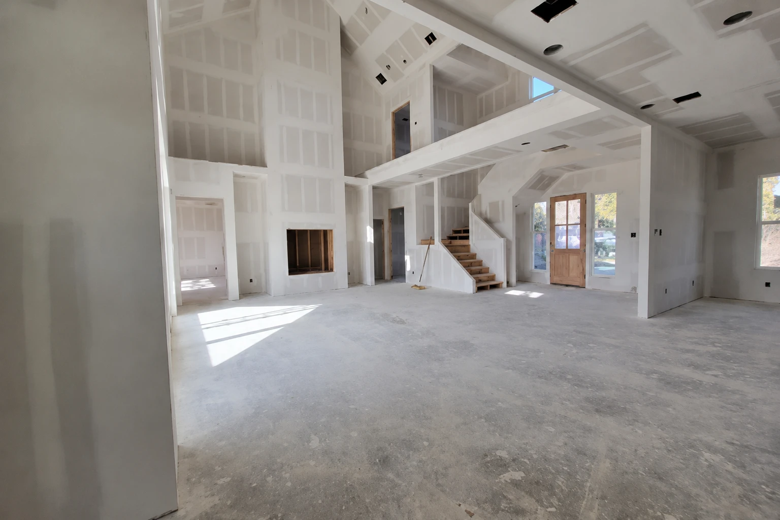 Drywalled great room with a staircase awaiting owner finish-out under the sweat equity program
