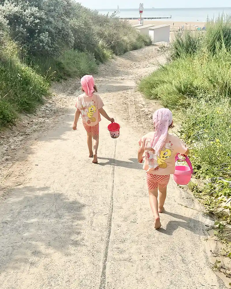 Zwei Kinder laufen mit Sandeimern den Dünenweg zum Strand hinunter