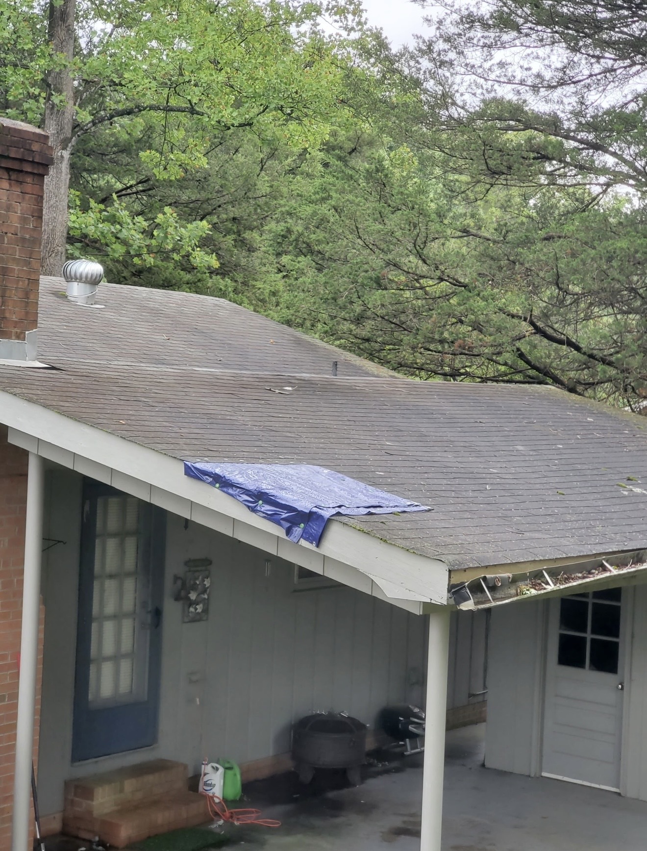Storm-damage cleanup with protective tarp and equipment at a residential property.