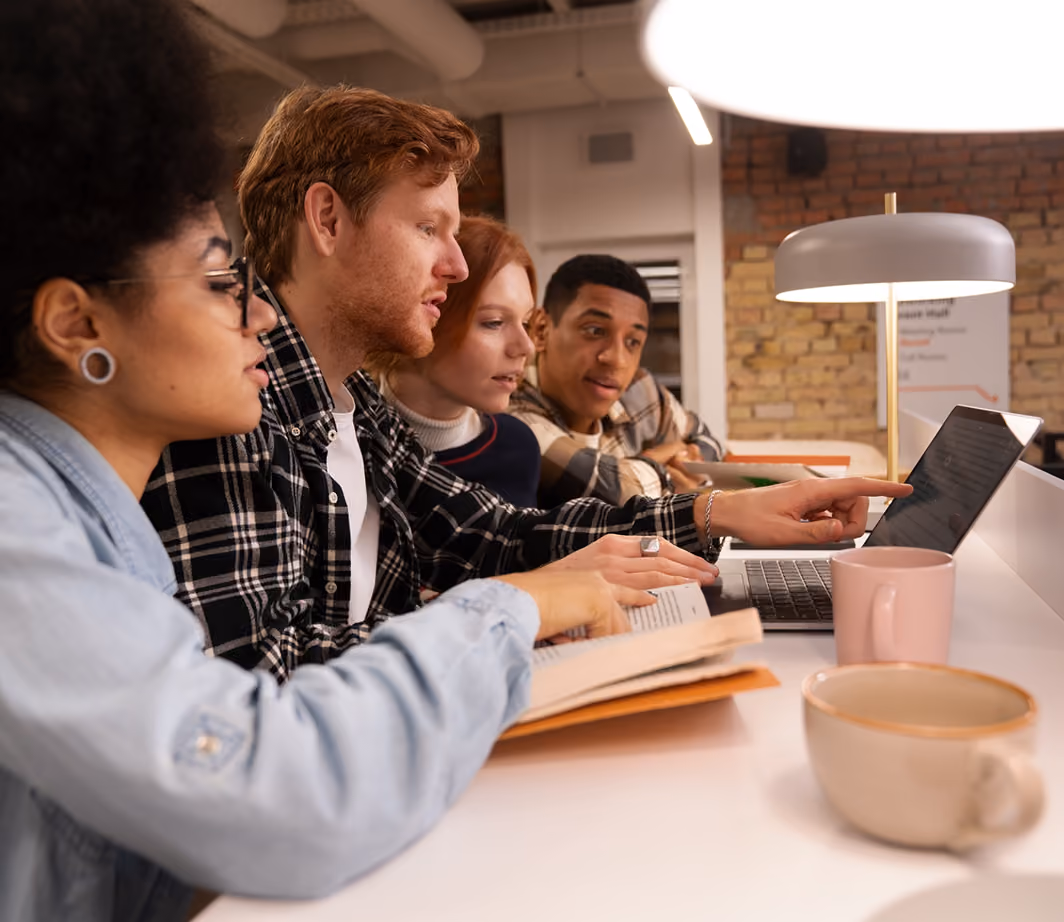 Young people studying together around a table with a laptop and books