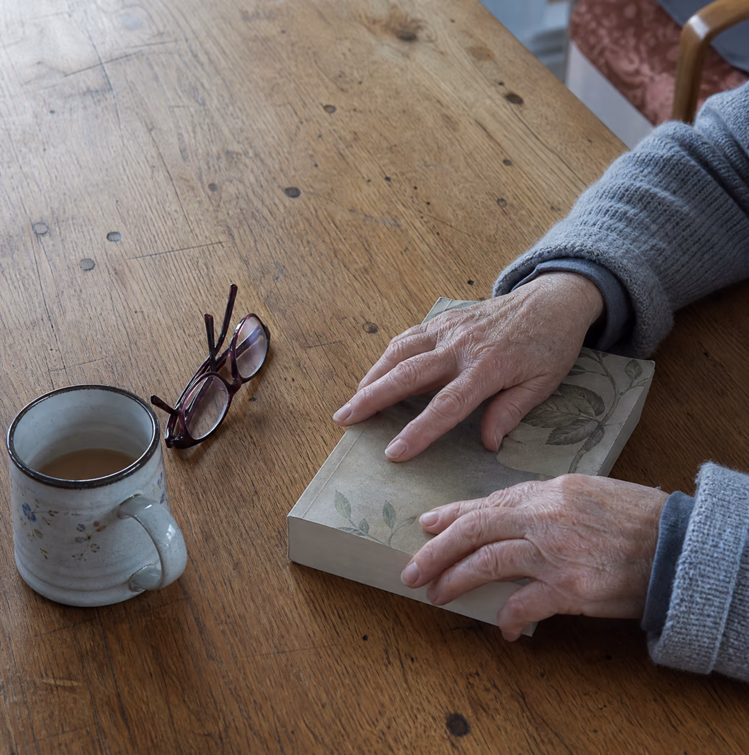 Hands resting on a book beside a mug and reading glasses