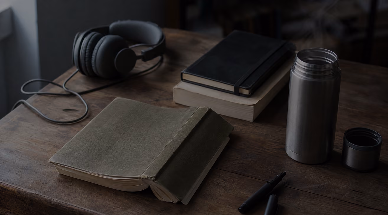 Headphones, notebooks and a flask on a dark wooden desk