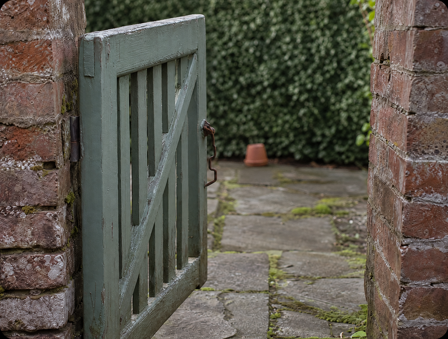 Old green garden gate opening onto a paved path