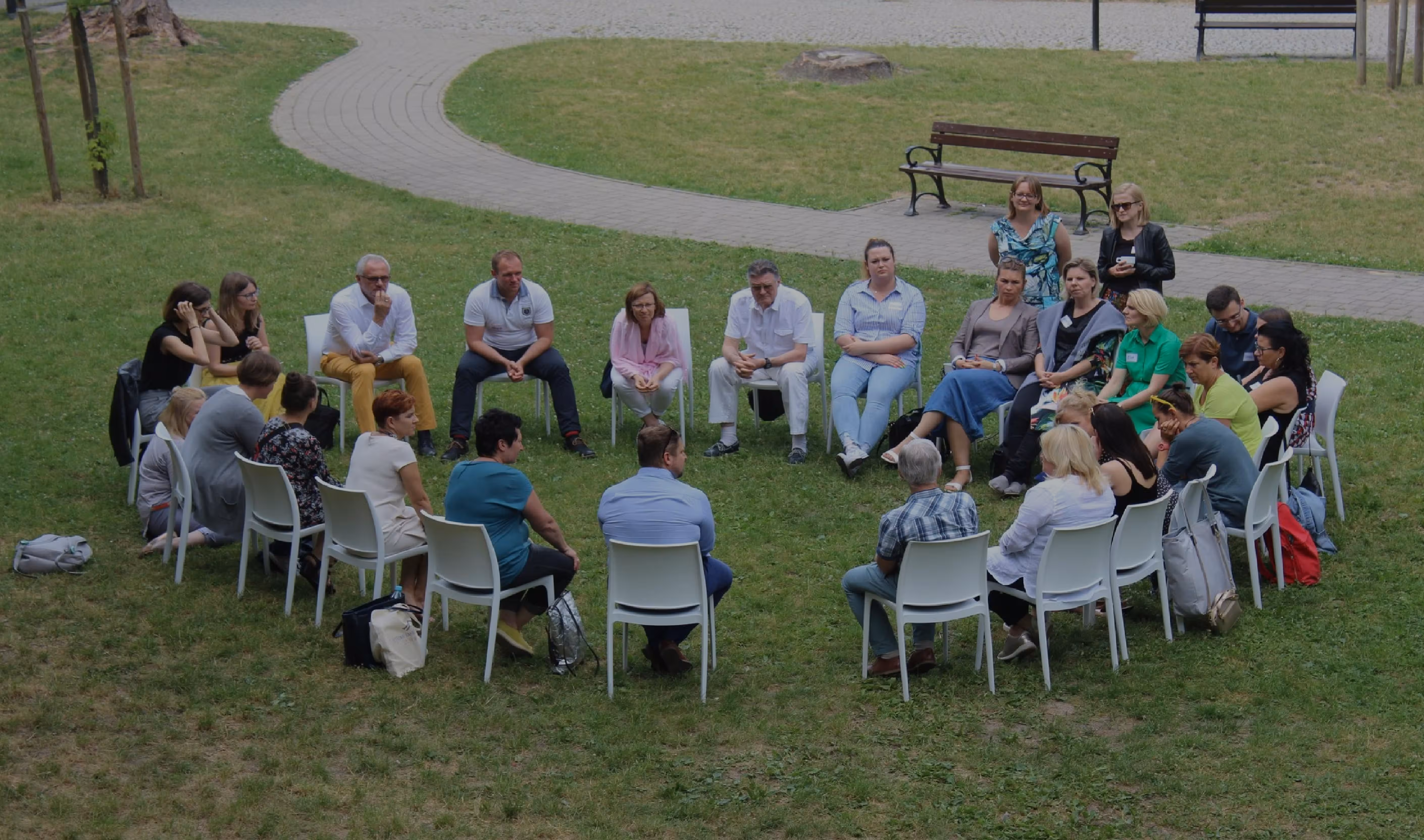 Climate café listening circle: a large group sitting in a circle of chairs on a park lawn