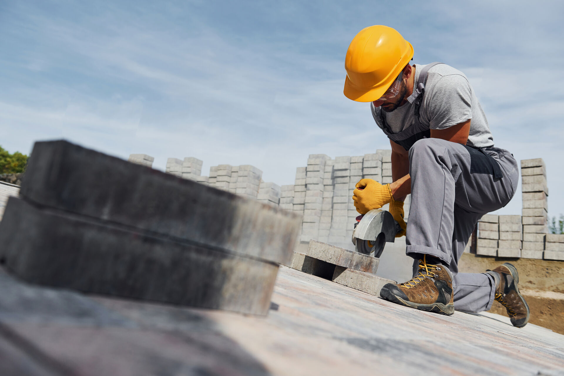 A construction worker wearing protective equipment cuts concrete paving stones with a power saw at an outdoor job site.
