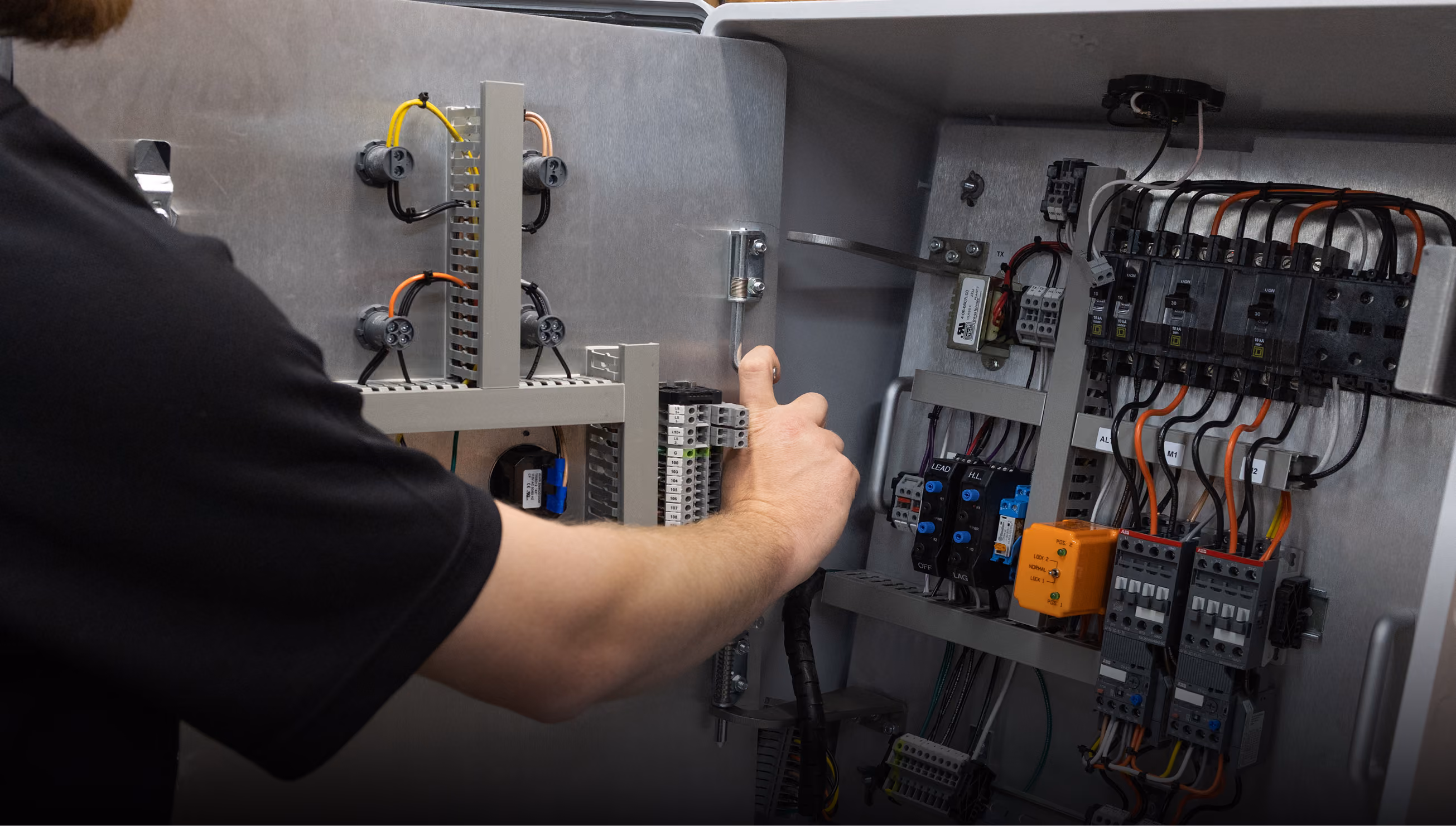 Person working on an open electrical control panel with wiring and circuit breakers.