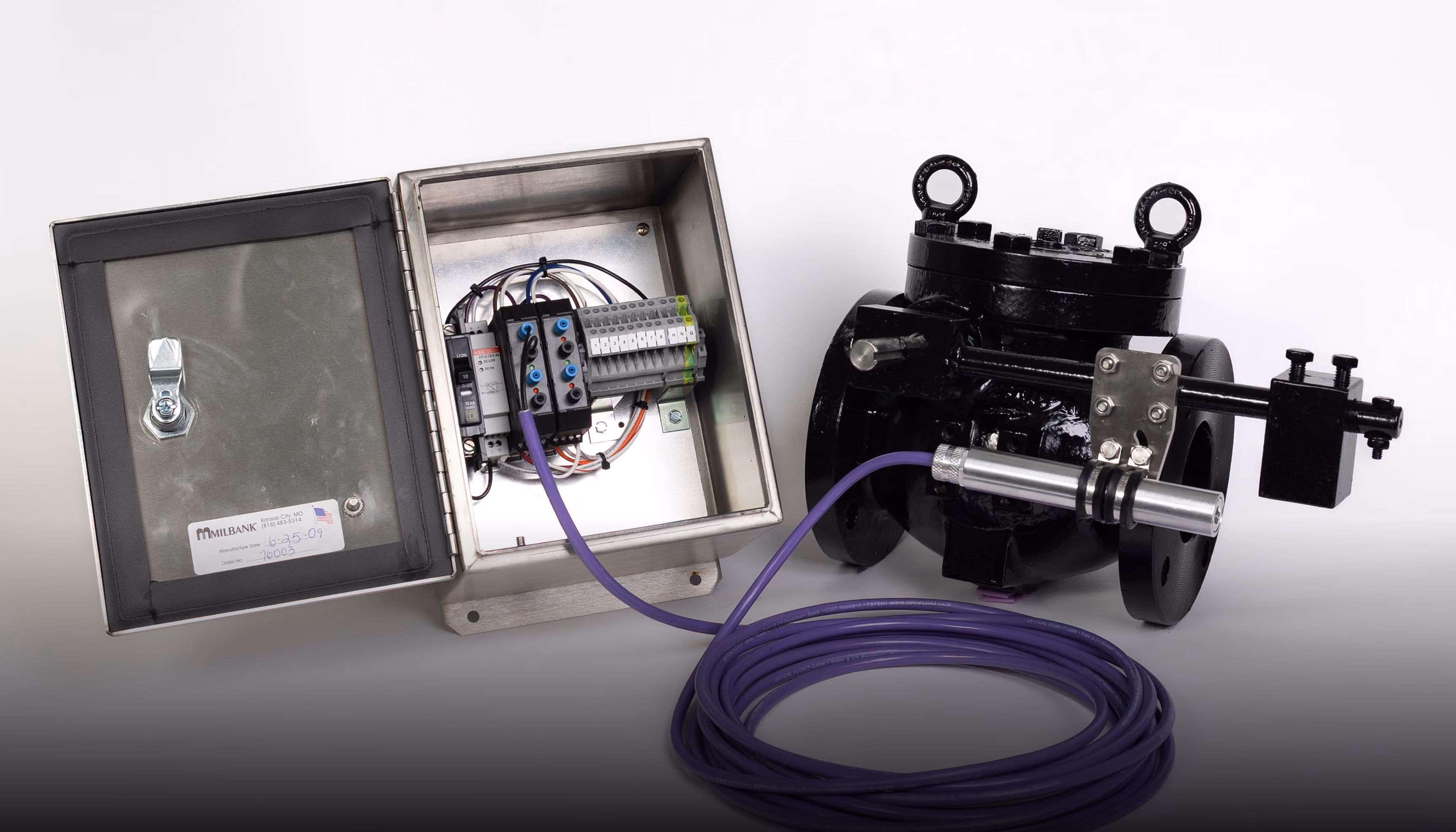 Industrial flow sensor with black valve and connected metal control box with wiring and purple cable coiled.