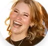 Smiling woman with curly blond hair wearing a black top and large hoop earrings.