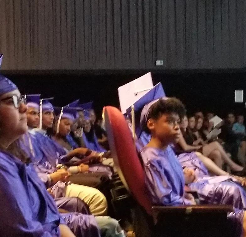 Students in blue caps and gowns seated at graduation ceremony