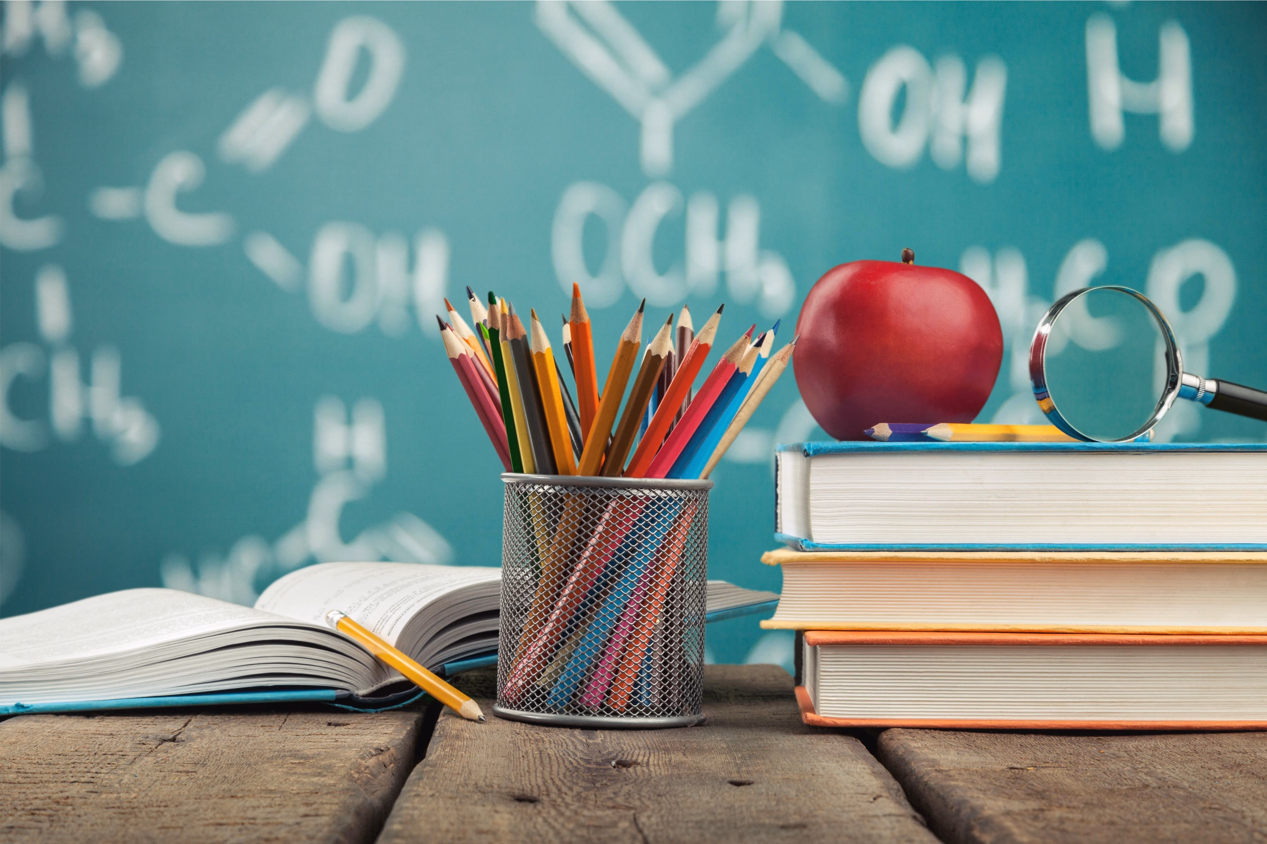 School supplies including colored pencils books and apple on desk