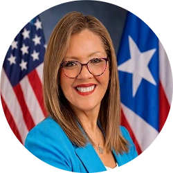 Official portrait of Irma J. Rosario in a blue blazer with U.S. and Puerto Rico flags behind her.