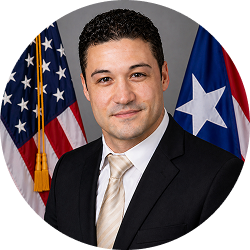 Official portrait of Ezequiel Nieves in a dark suit and light tie, with U.S. and Puerto Rico flags behind him.