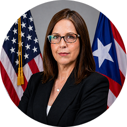 Official portrait of Iraida Mejías Arroyo in glasses and a black blazer, with U.S. and Puerto Rico flags behind her.