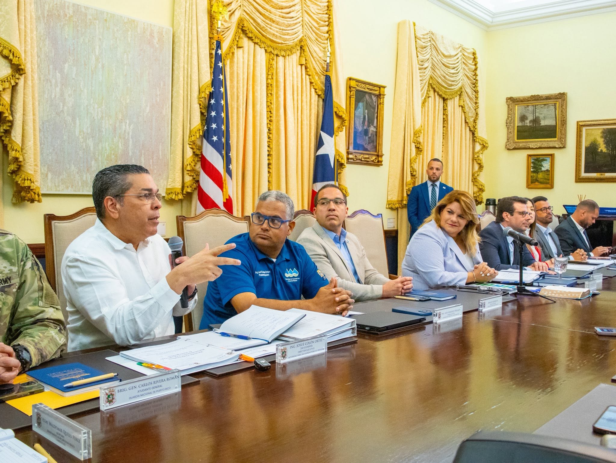 Eng. Josué A. Colón Ortiz speaks during a government meeting at government offices, seated with Governor Jenniffer González Colón, officials, and staff.