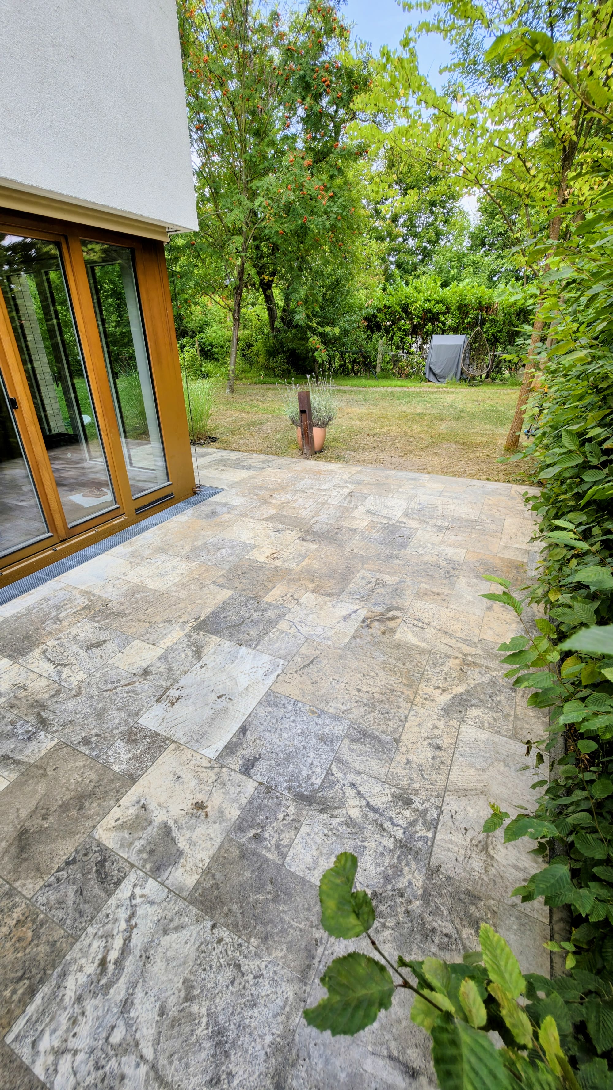 Fertige Travertin-Terrasse mit Wintergarten und angrenzendem Garten